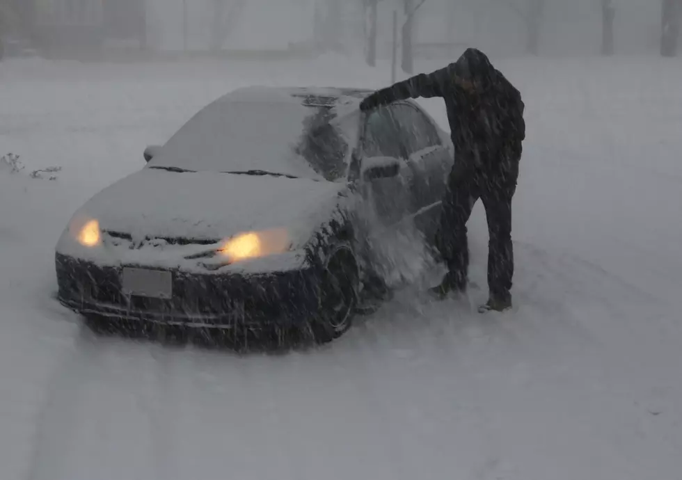 A man clearing snow off of a car during a blizzard.